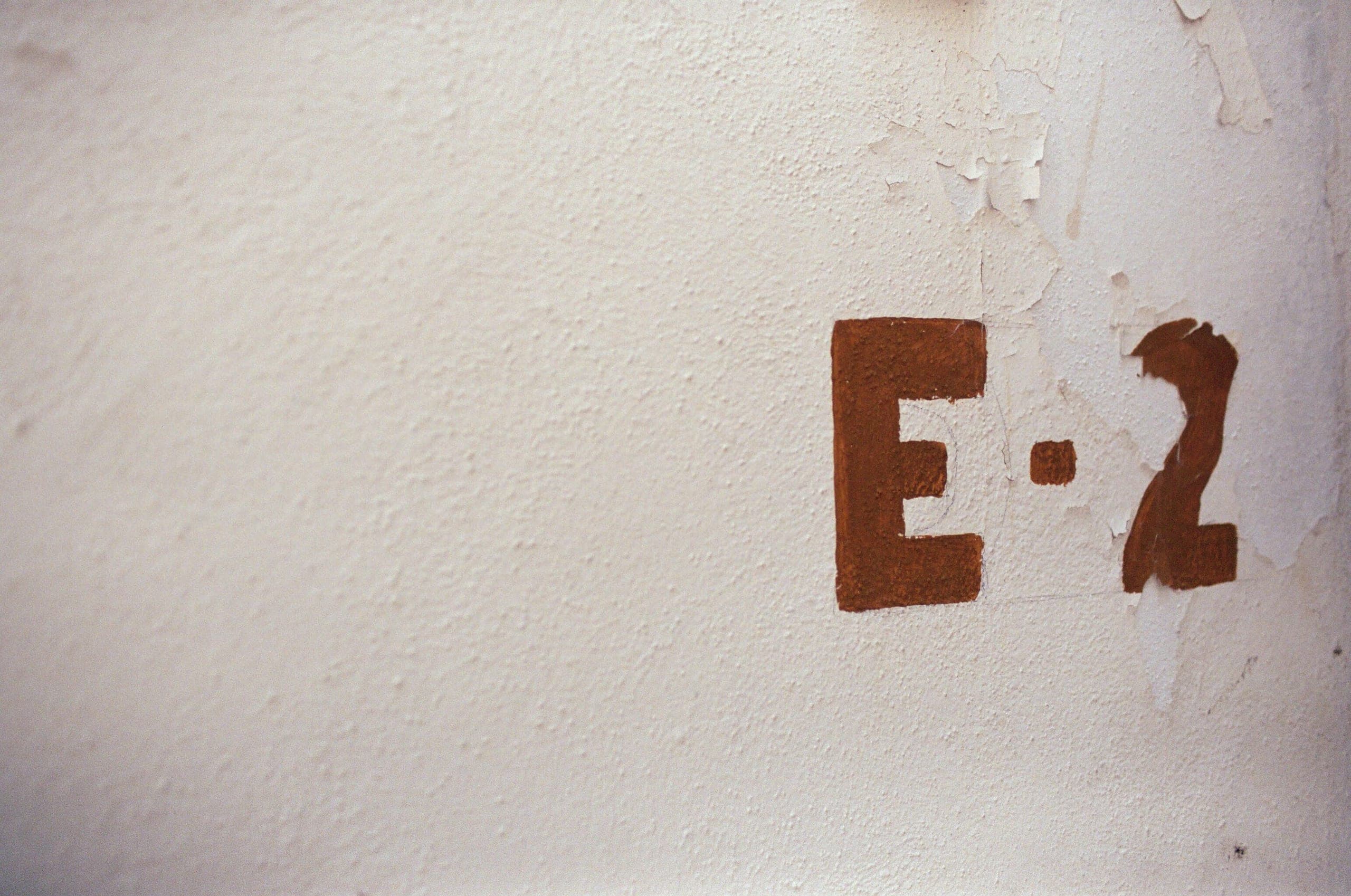 Rust-colored hand-painted E·2 on a textured white plaster wall