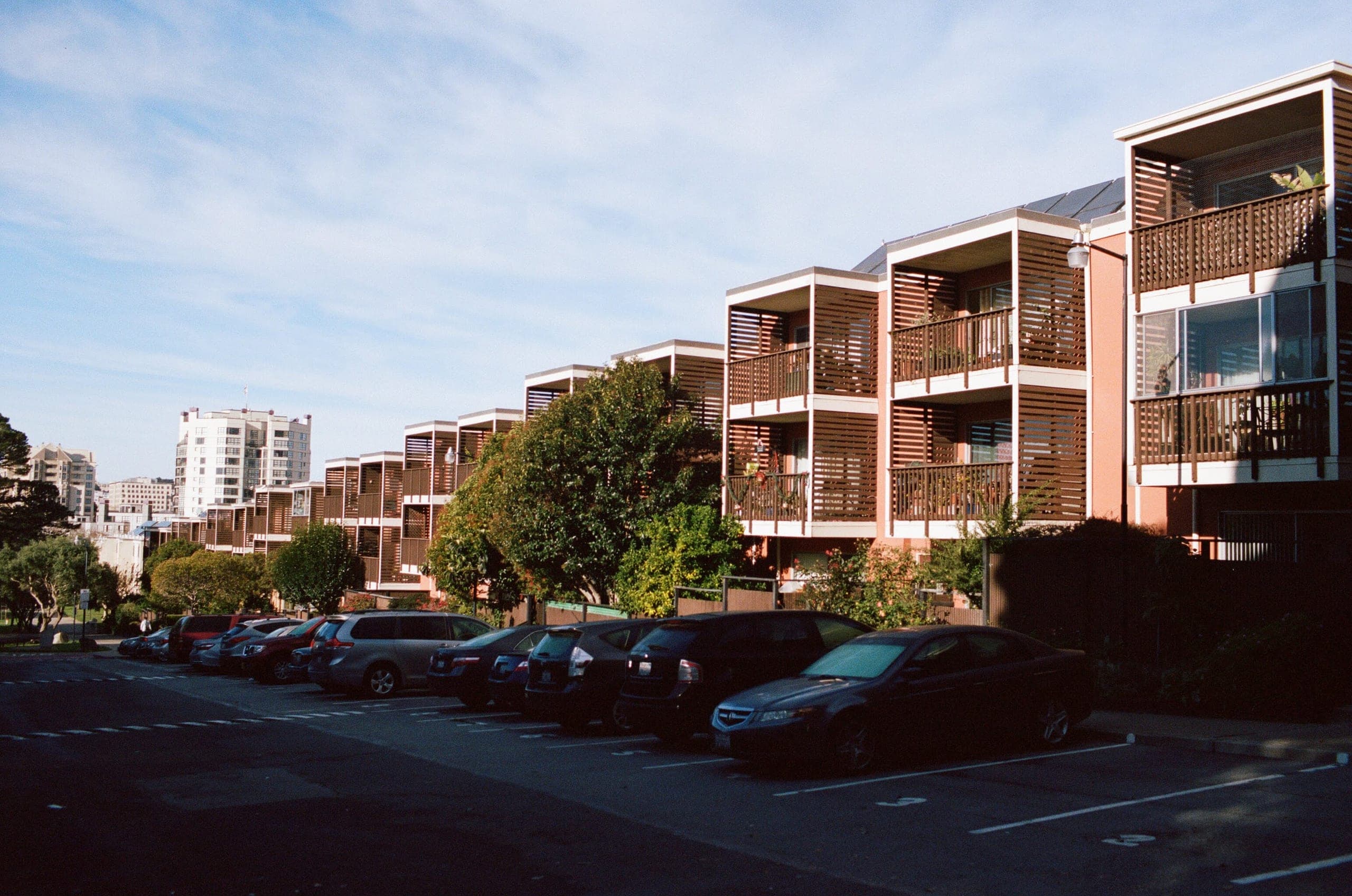 Row of brown wood-slat balconies on condos with a parking lot in front