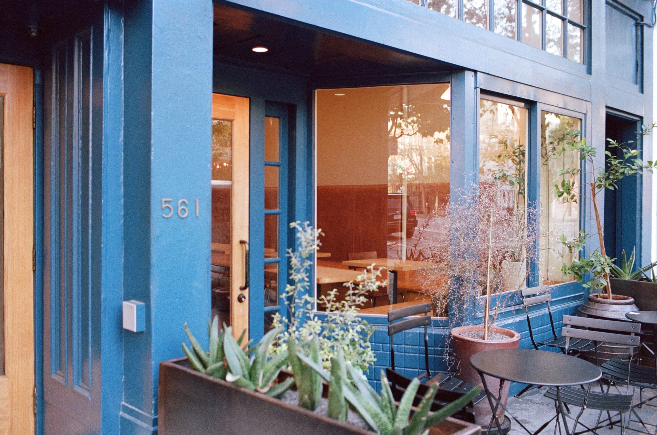 Blue painted storefront with the number 561, succulents in a planter and outdoor seating