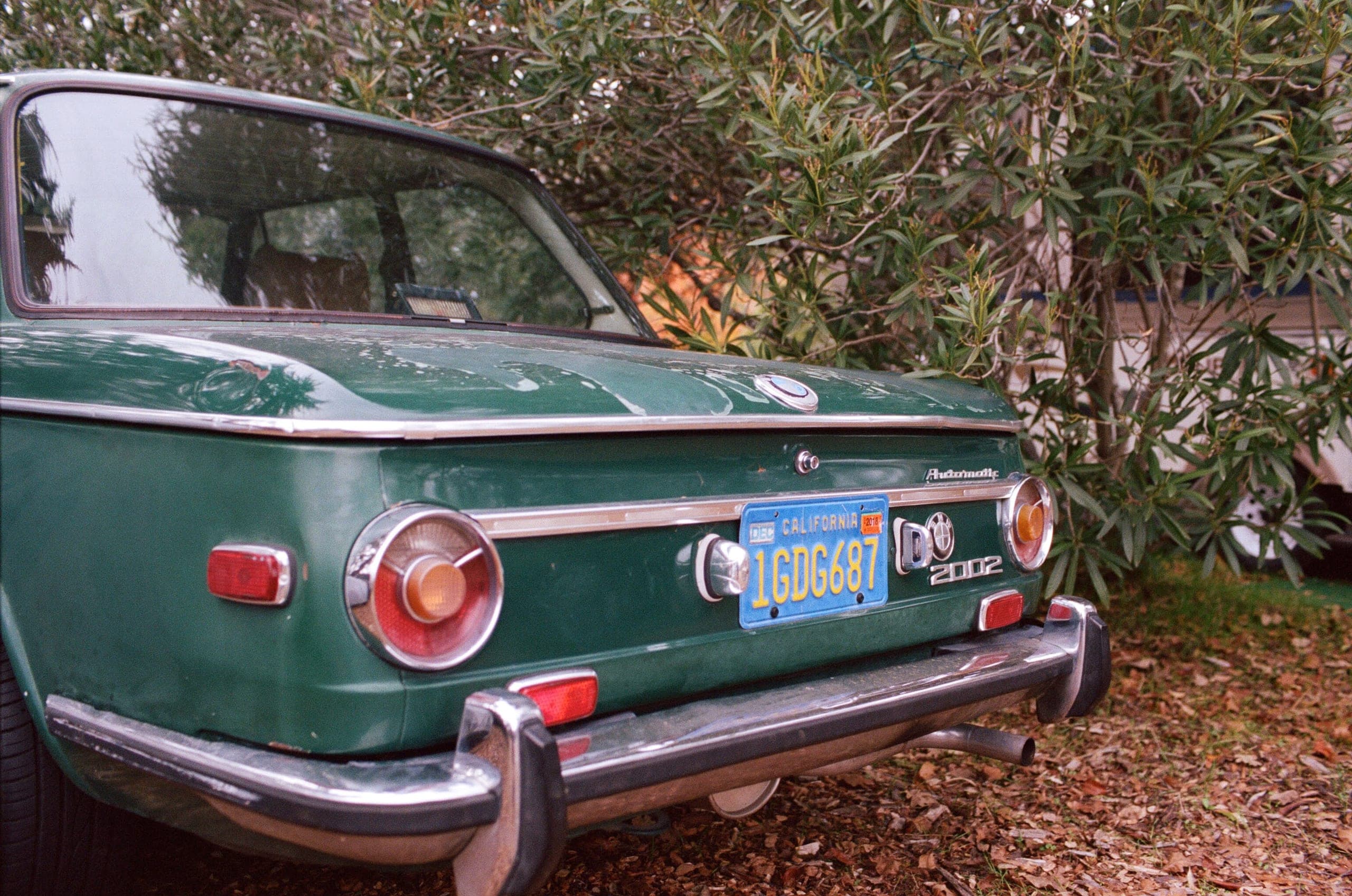Rear three-quarter of a green BMW 2002 Automatic parked next to bushes
