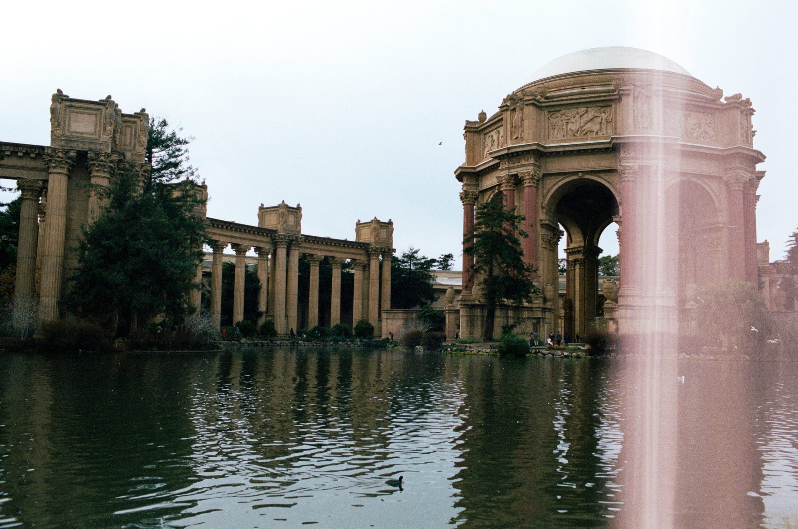 Palace of Fine Arts dome and colonnade reflected in the lagoon, with a pink vertical light streak