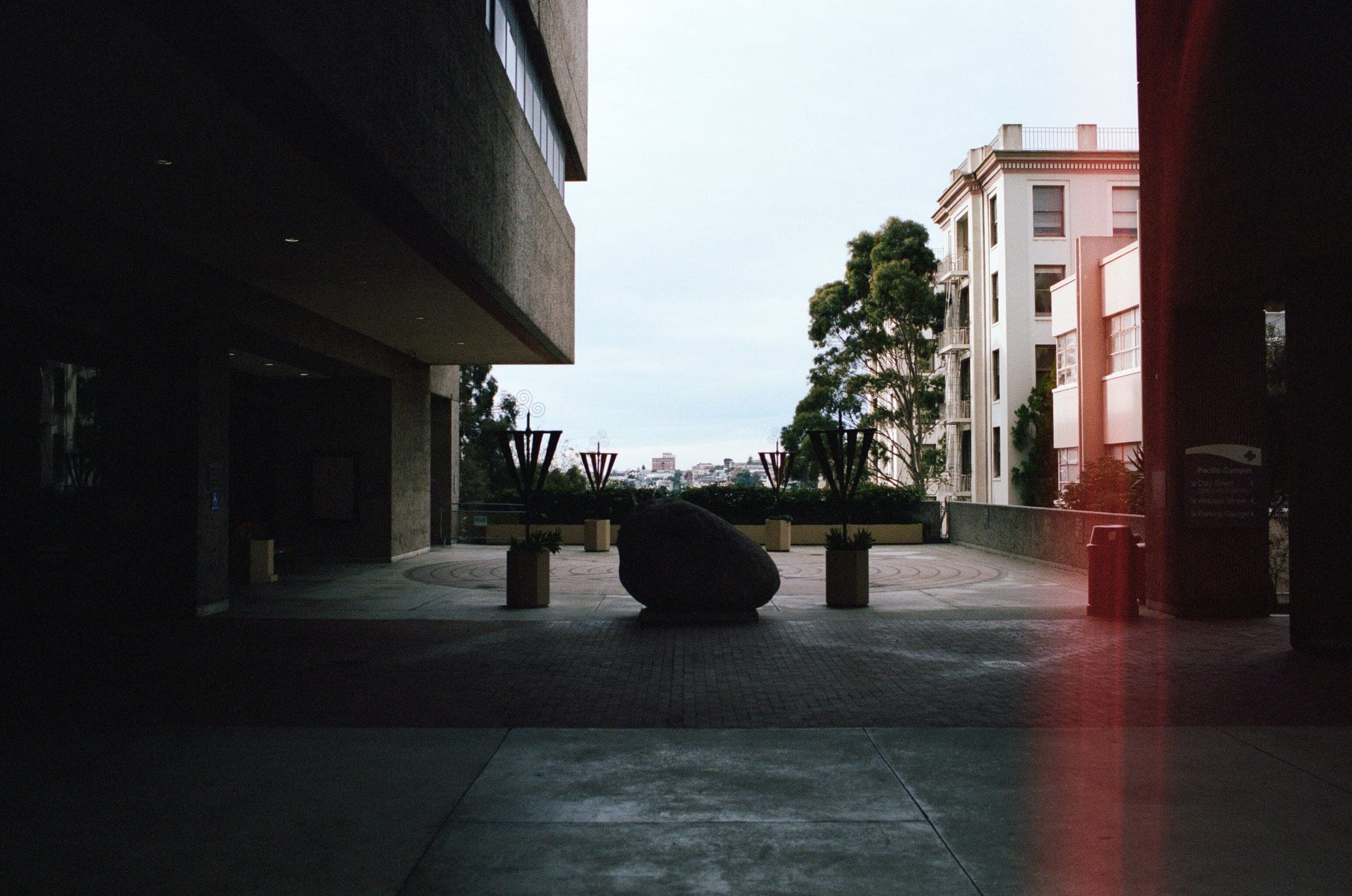 Modern plaza with a rock sculpture and a large pink light leak on the right