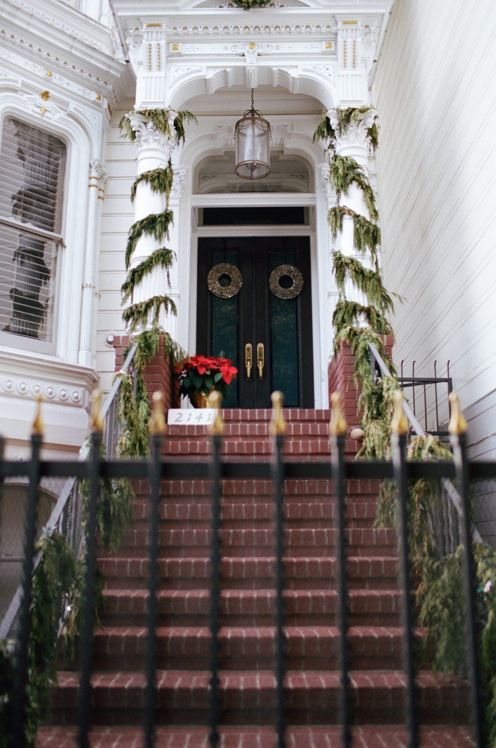 White Victorian with green double doors covered in cedar garlands and brass wreaths